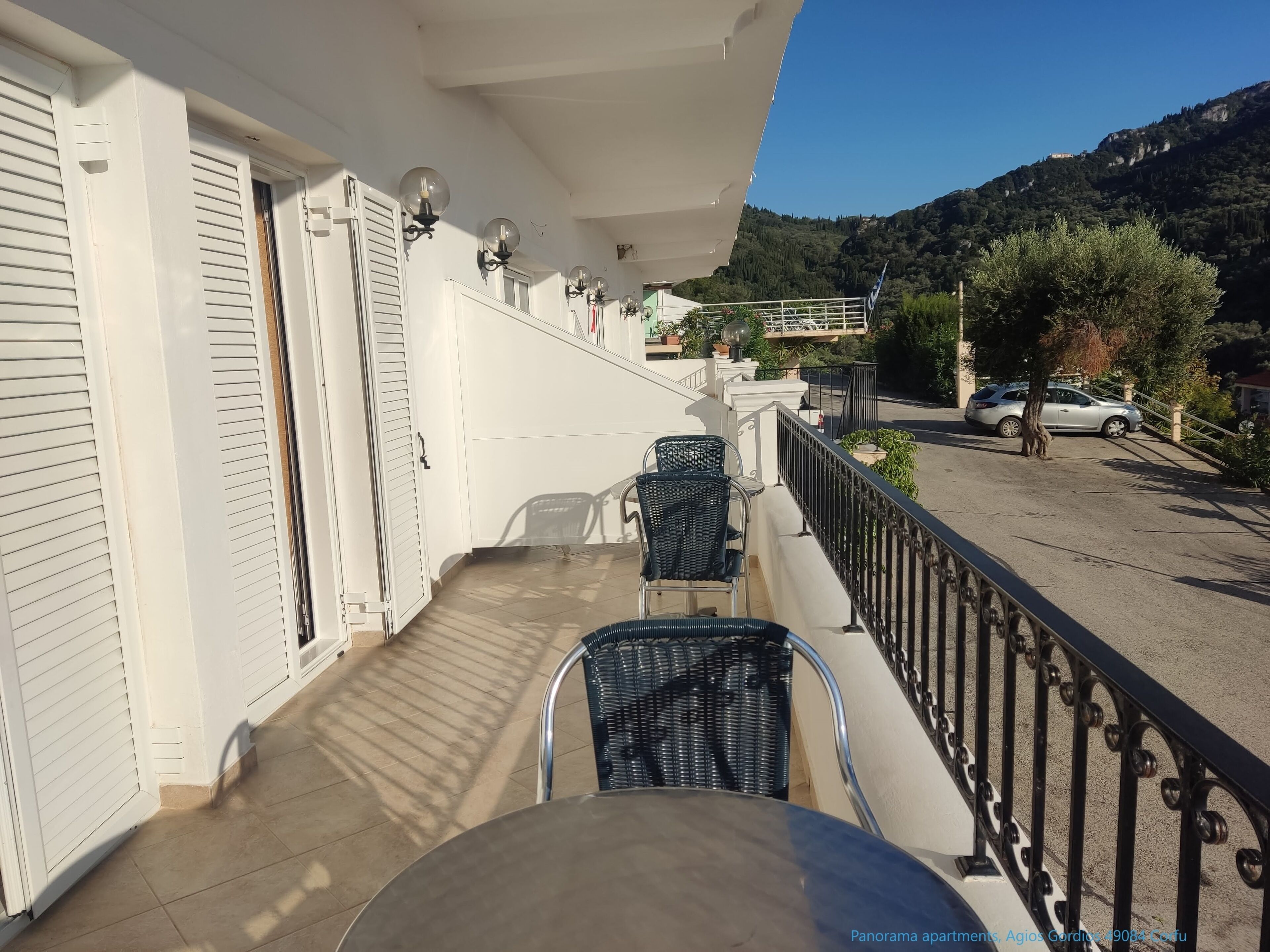 Un balcón con dos sillas y una mesa, con vistas a una calle y un paisaje montañoso.