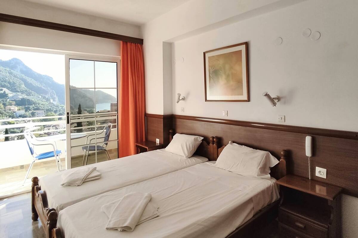 A hotel room with a large bed, a bedside table, a phone, and a painting on the wall.