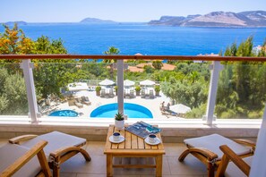 A balcony with a wooden table, two cushioned chairs, and a view of a swimming pool and the sea. - Olea Nova Hotel (Kas)