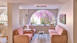 Une pièce chaleureuse avec un canapé rose, une petite table et une grande fenêtre donnant sur un jardin de fleurs roses.