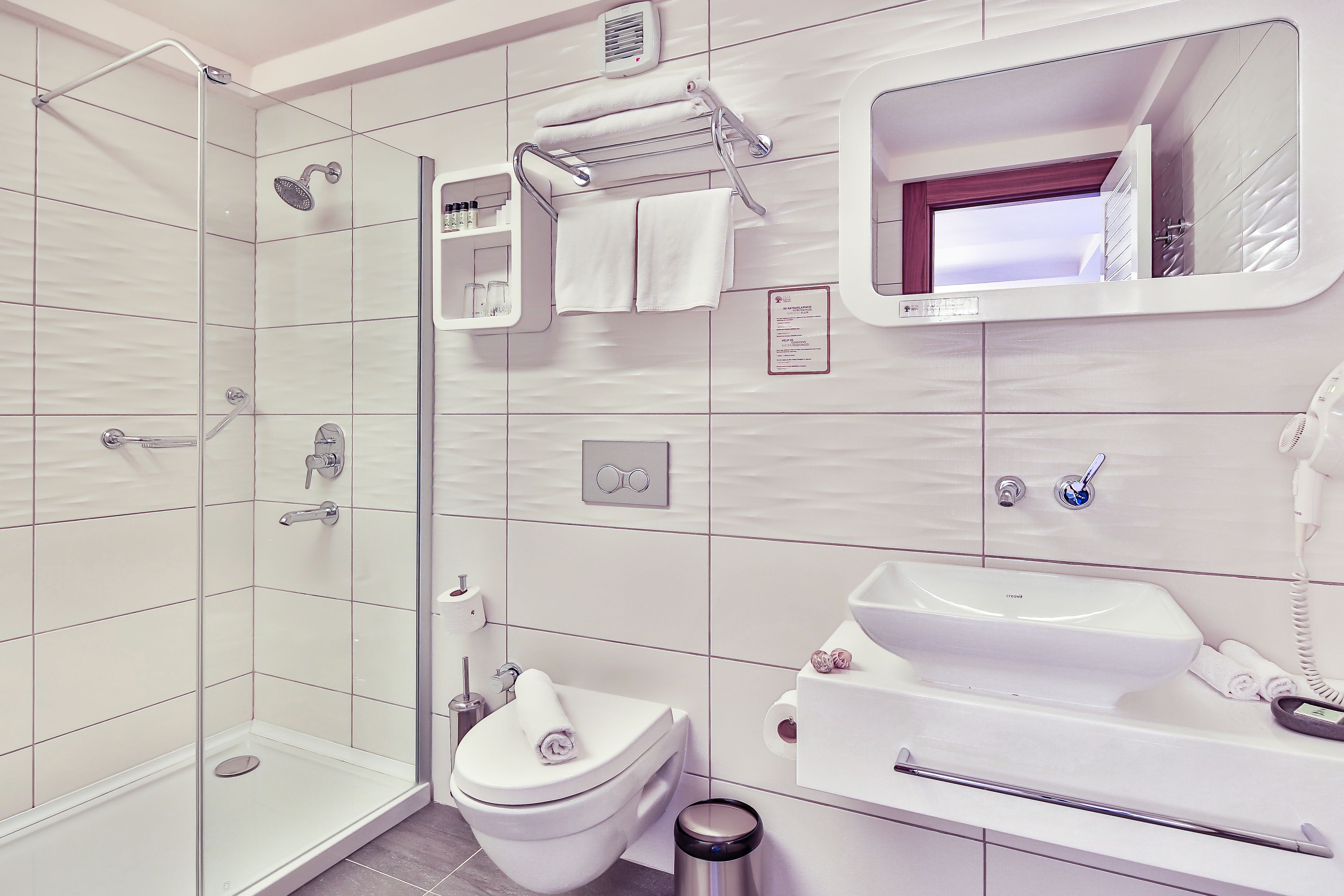 Un baño moderno con ducha de vidrio, inodoro blanco, lavabo y espejo.