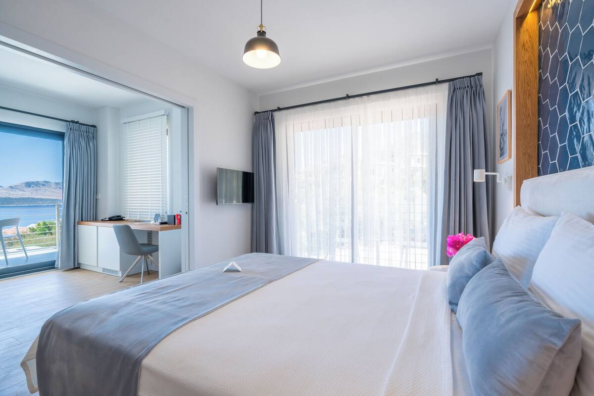 A modern hotel room with a large bed, a desk, and a view of the sea.