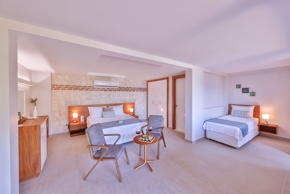 A modern hotel room with a large bed, two bedside tables, a small dining table, and a seating area with chairs.