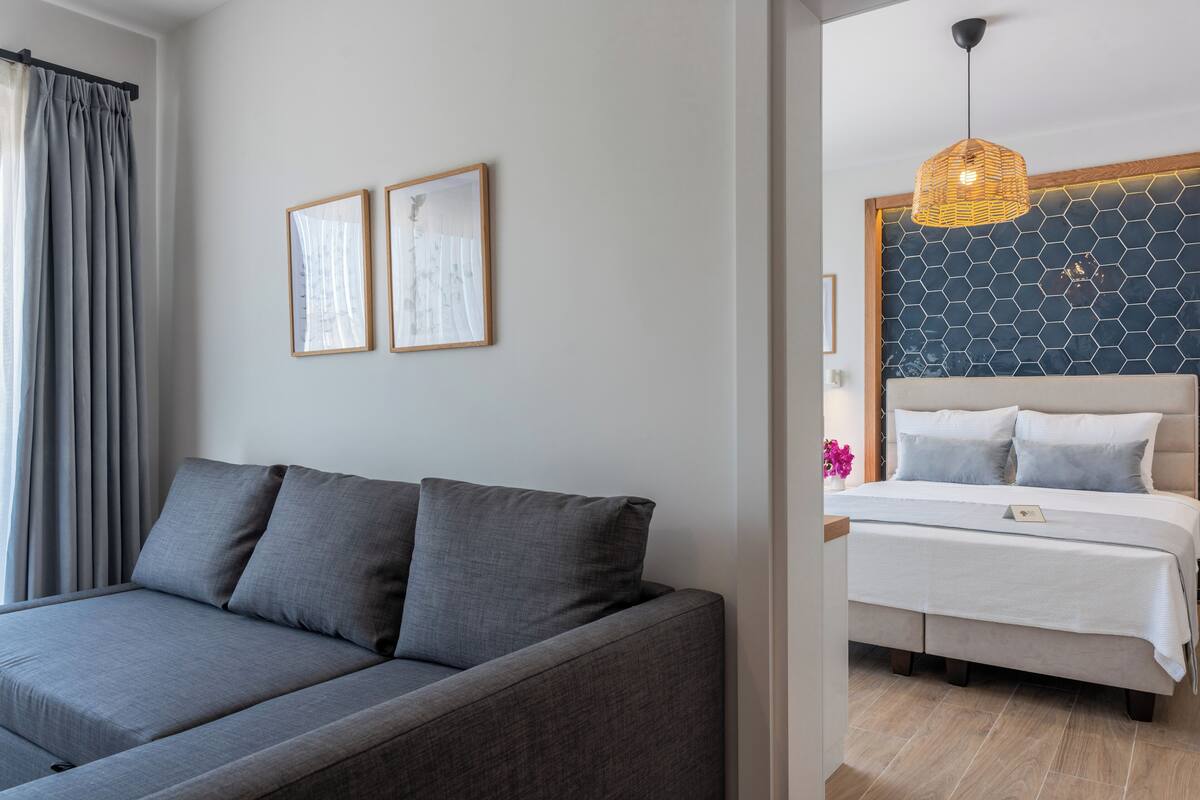 A modern bedroom with a grey sofa, a bed with white bedding, and a hexagonal patterned wall.