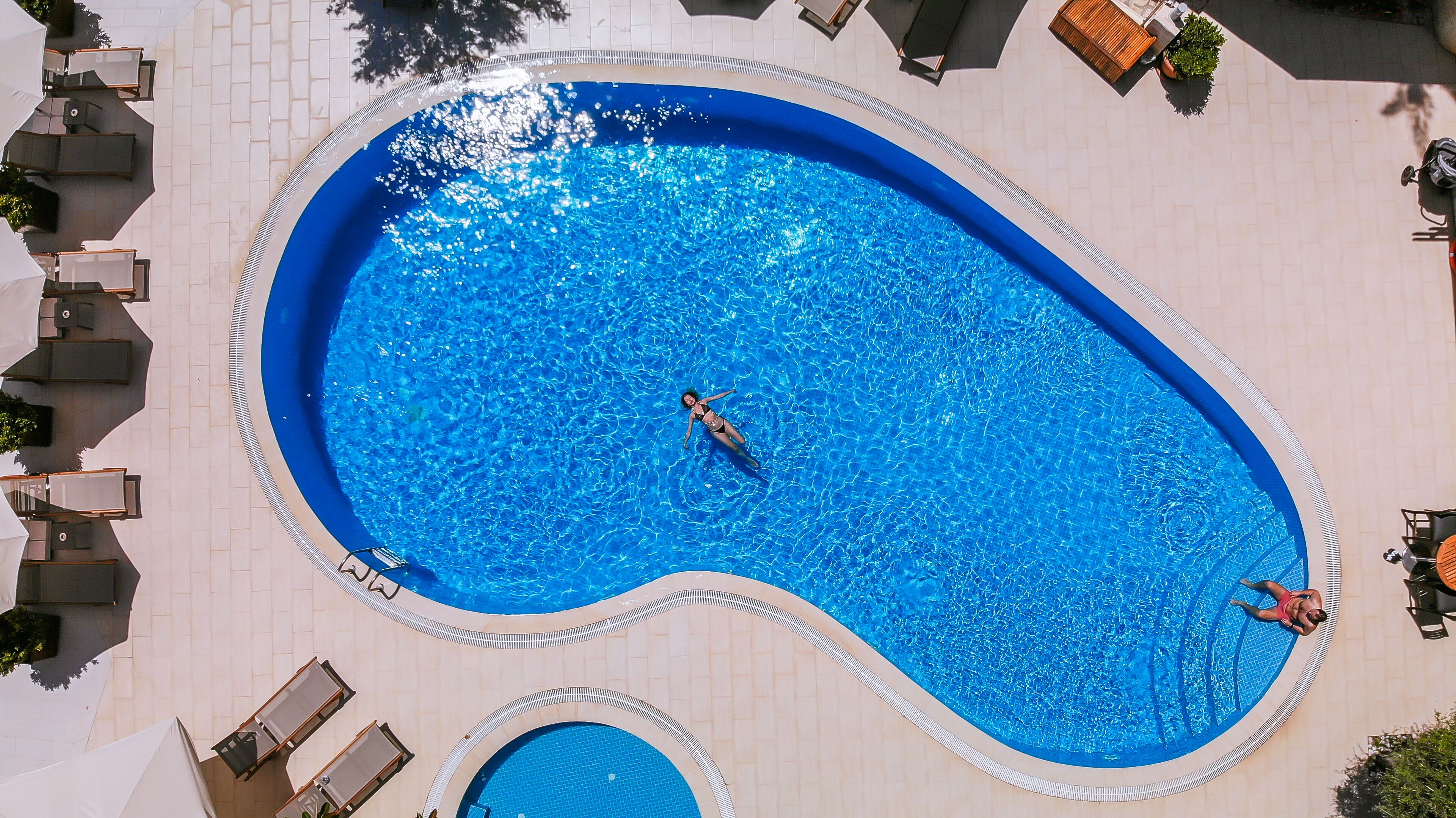 Une grande piscine de forme ovale, à l’eau d’un bleu limpide, entourée de chaises longues et bordée d’une terrasse carrelée.