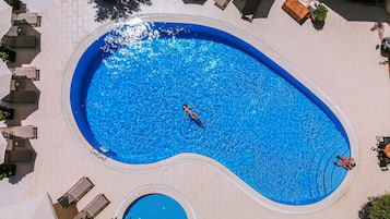 Une grande piscine de forme ovale, à l’eau d’un bleu limpide, entourée de chaises longues et bordée d’une terrasse carrelée.