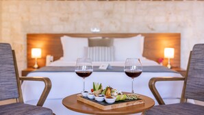 Une chambre d’hôtel avec un lit, deux lampes de chevet, une petite table sur laquelle se trouve un plateau avec de la nourriture et deux verres de vin rouge.