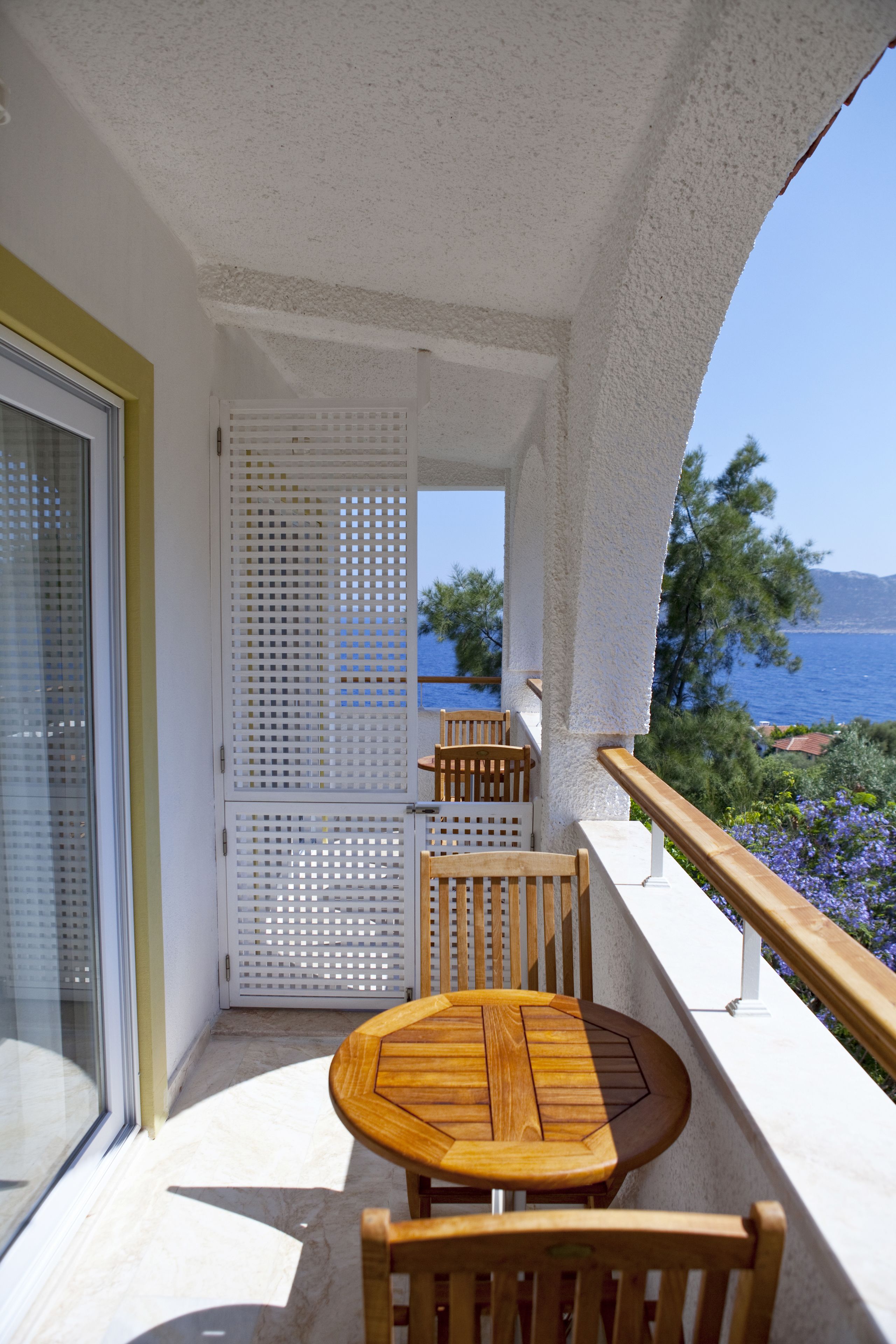 Un balcón con mesa y sillas de madera, una puerta blanca y vista al mar.
