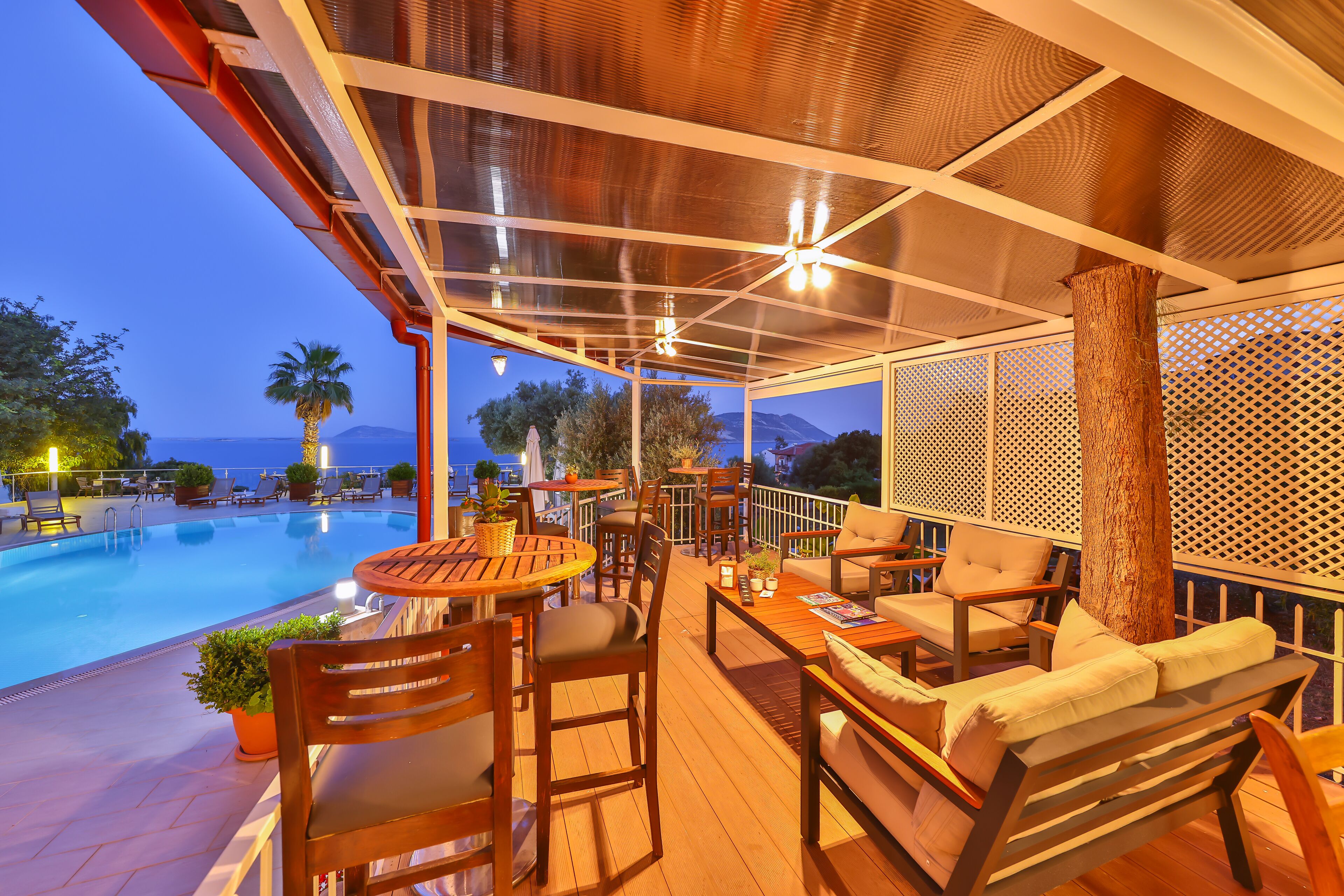 A poolside area with wooden furniture, a covered seating area, and a view of the pool and mountains.