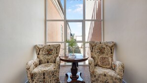 A corner room with two floral armchairs, a round wooden table, and a large window with a view of buildings. - Hotel Postgaarden (Fredericia)