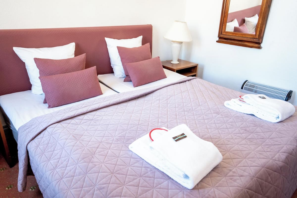 A neatly made bed with a quilted cover, pillows, and a folded towel on the bed.
