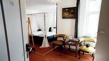 A room with a bed, a chair, a small table, a radiator, and a painting on the wall.