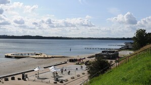 A beach with a pier, a small building, and a grassy area. - Hotel Postgaarden (Fredericia)