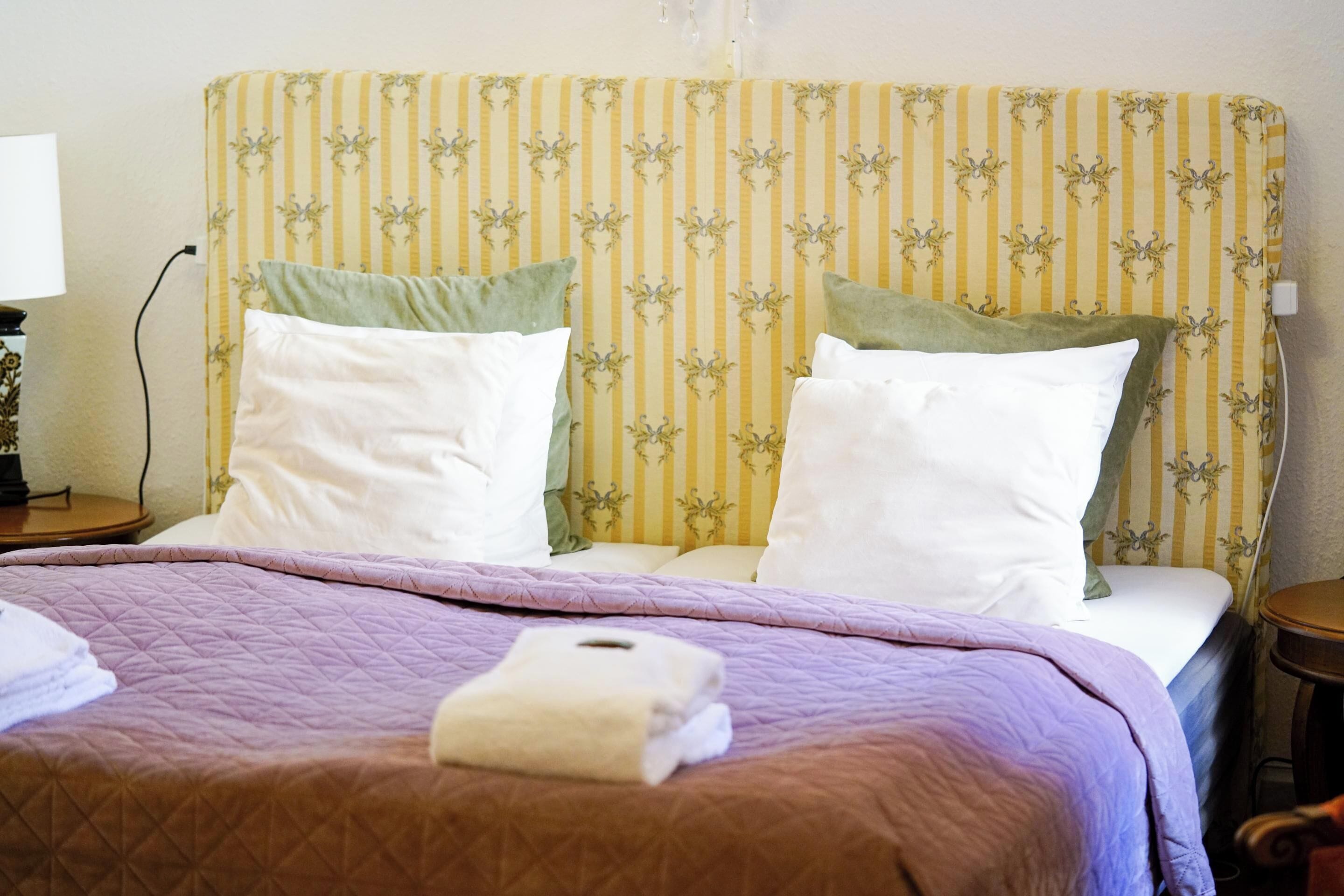 Una cama bien hecha con un cabecero a rayas, una colcha morada y dos almohadas.
