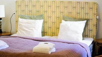 Una cama bien hecha con un cabecero a rayas, una colcha morada y dos almohadas.