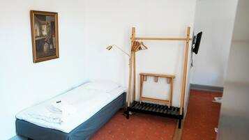A small, simple room with a single bed, a wooden rack, and a framed picture on the wall.