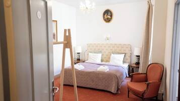 Una habitación de hotel con cama, una silla, un escritorio, una araña y un cuadro en la pared.