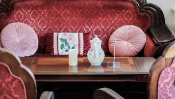 A wooden table with a white teapot and a cup, set on a red upholstered sofa with decorative pillows.