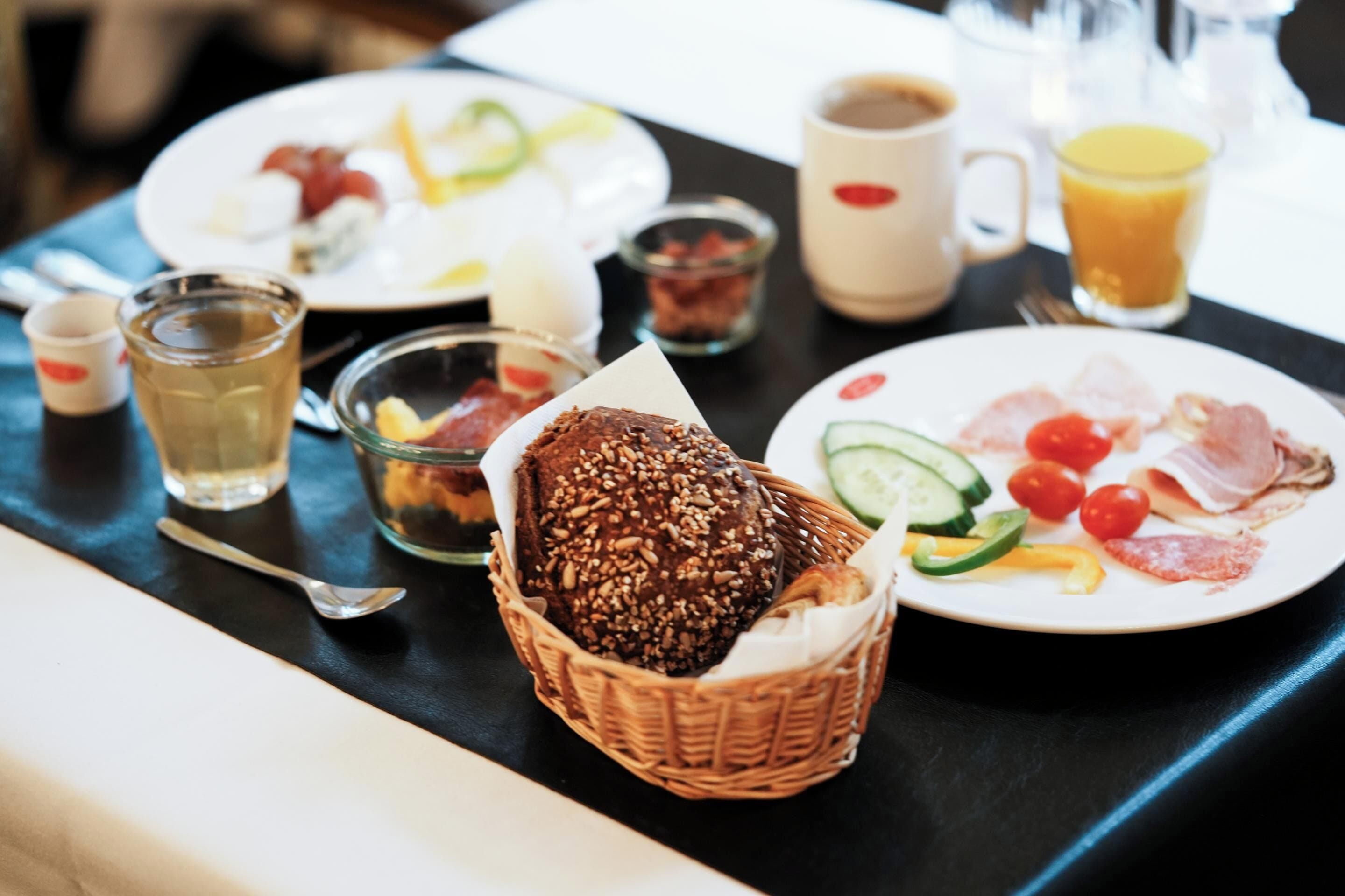 Una mesa de desayuno con platos de comida, una cesta de pan y un vaso de jugo.