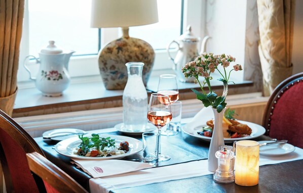 A dining table set with plates, glasses, a candle, and a vase with flowers. - Hotel Postgaarden (Fredericia)