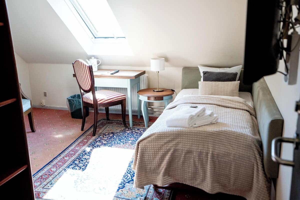 A bedroom with a bed, a desk, a chair, a lamp, and a window.