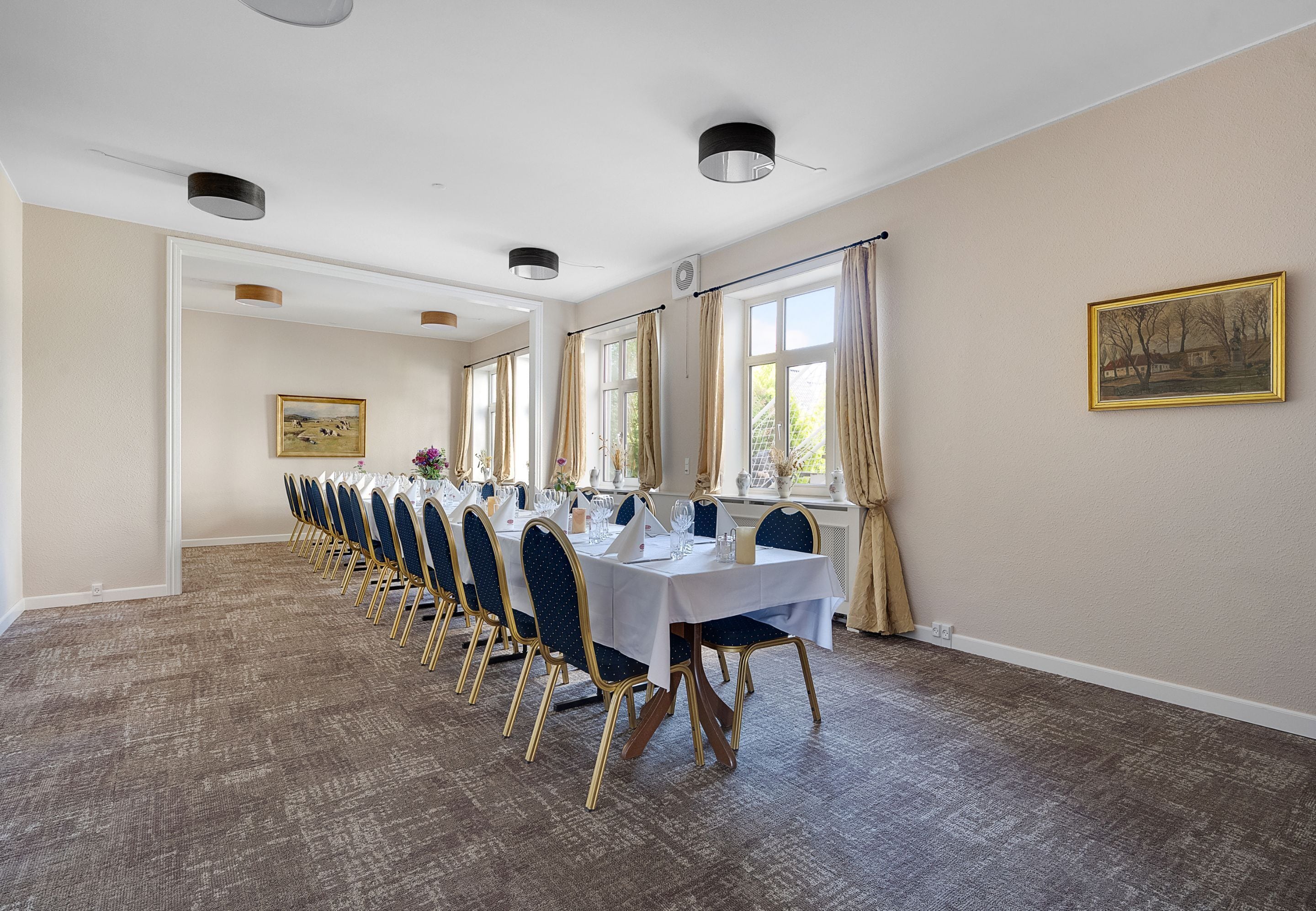 A long dining table with chairs, a white tablecloth, and a painting on the wall.