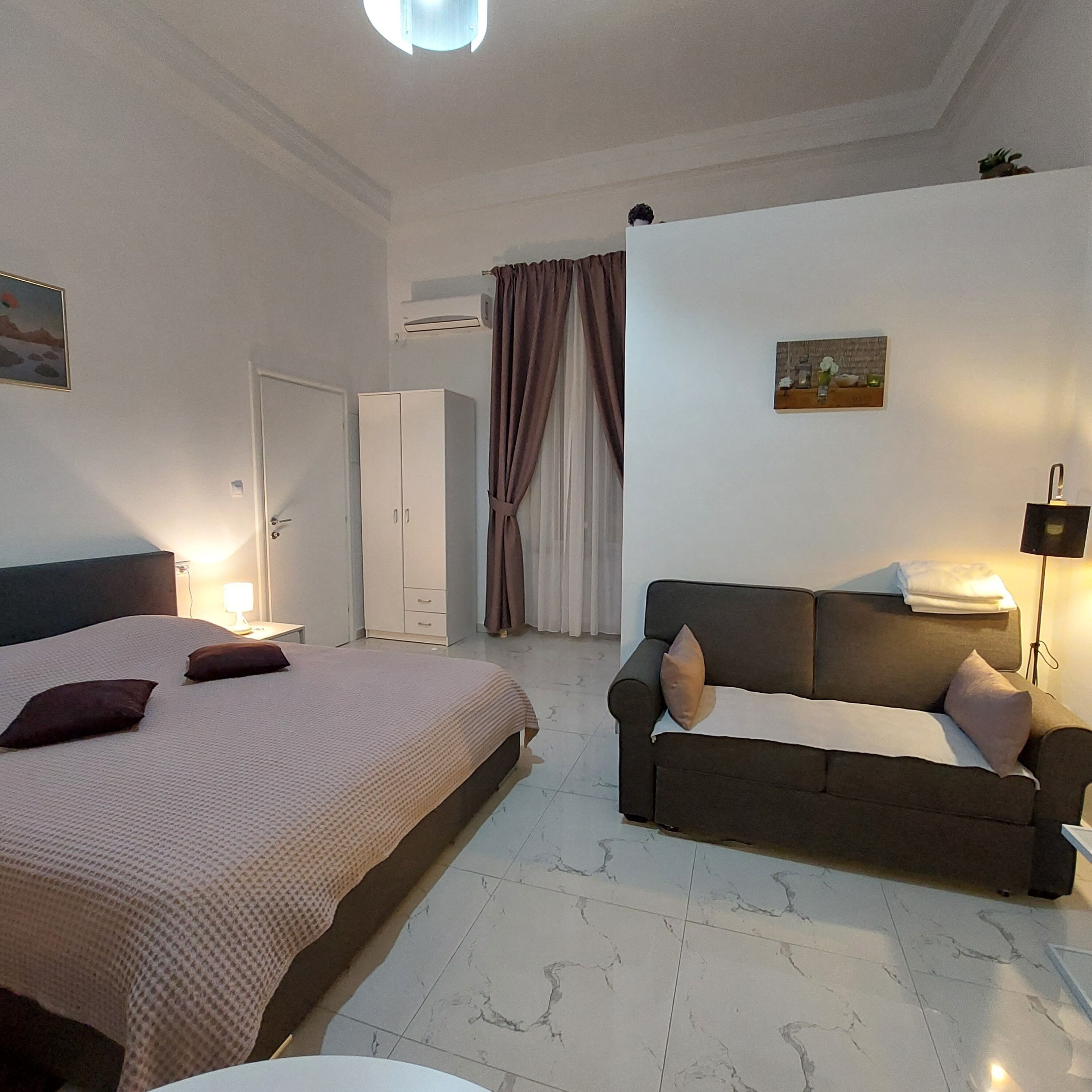 Un dormitorio con cama, sofá, mesita de noche y aire acondicionado de pared.