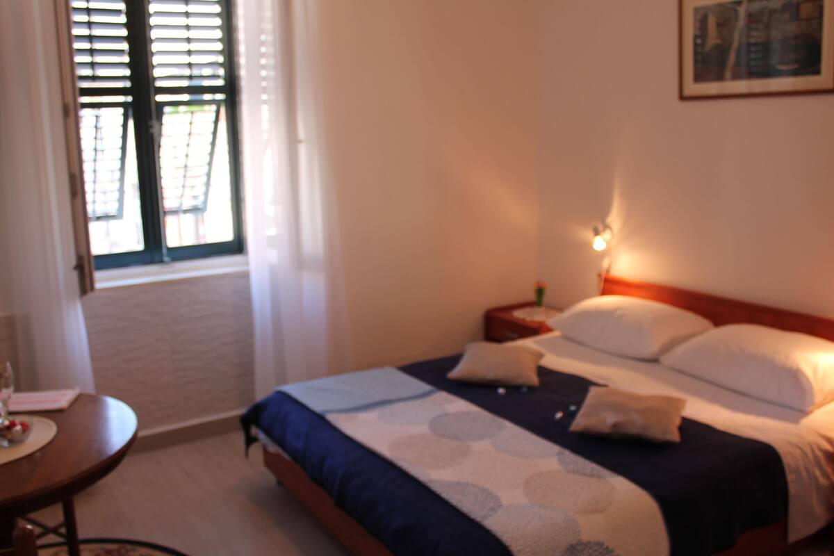 Un dormitorio con cama, mesita de noche, lámpara y ventana con persianas.