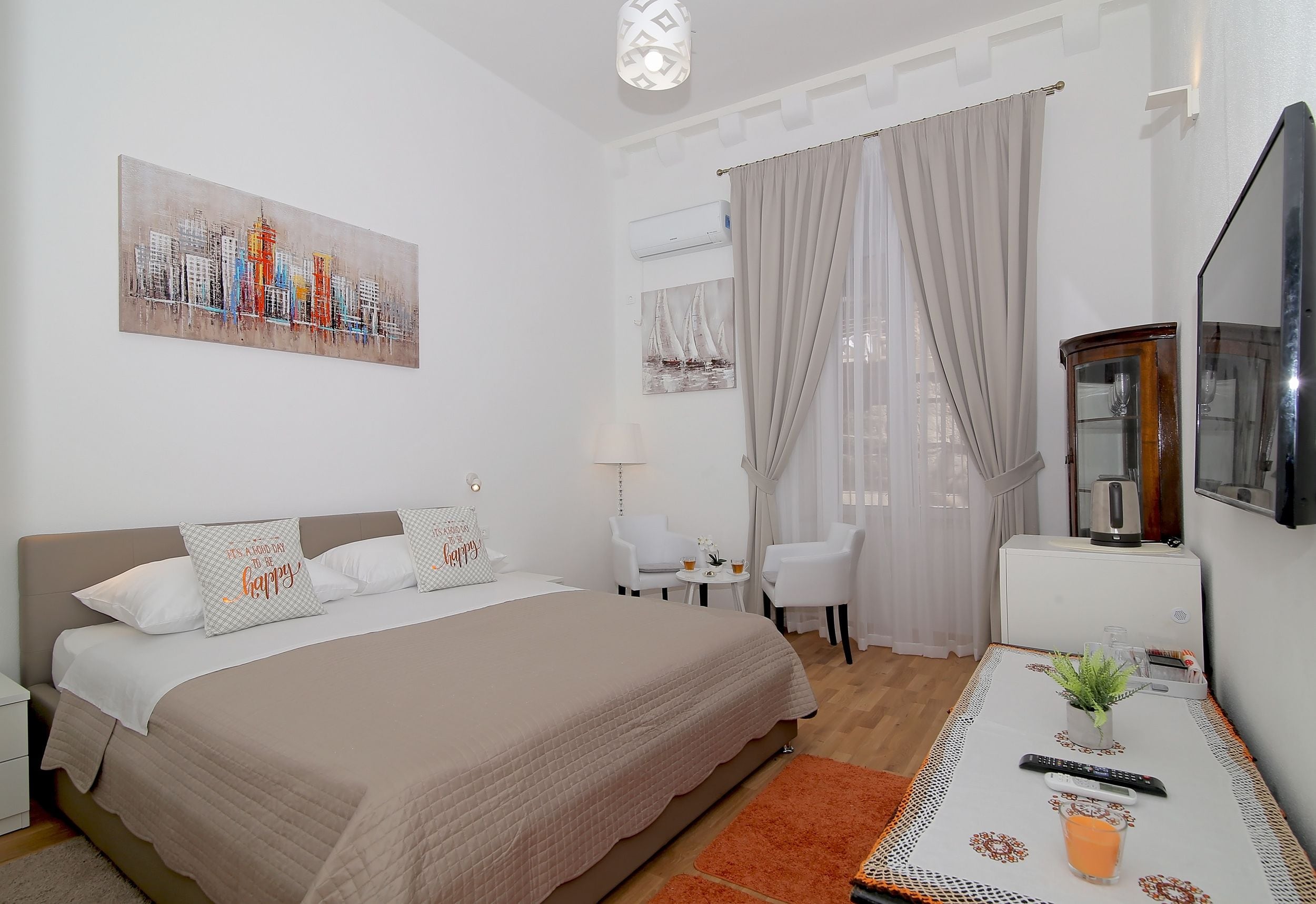 A modern hotel room with a large bed, a desk with a chair, a television, and a cityscape painting on the wall.
