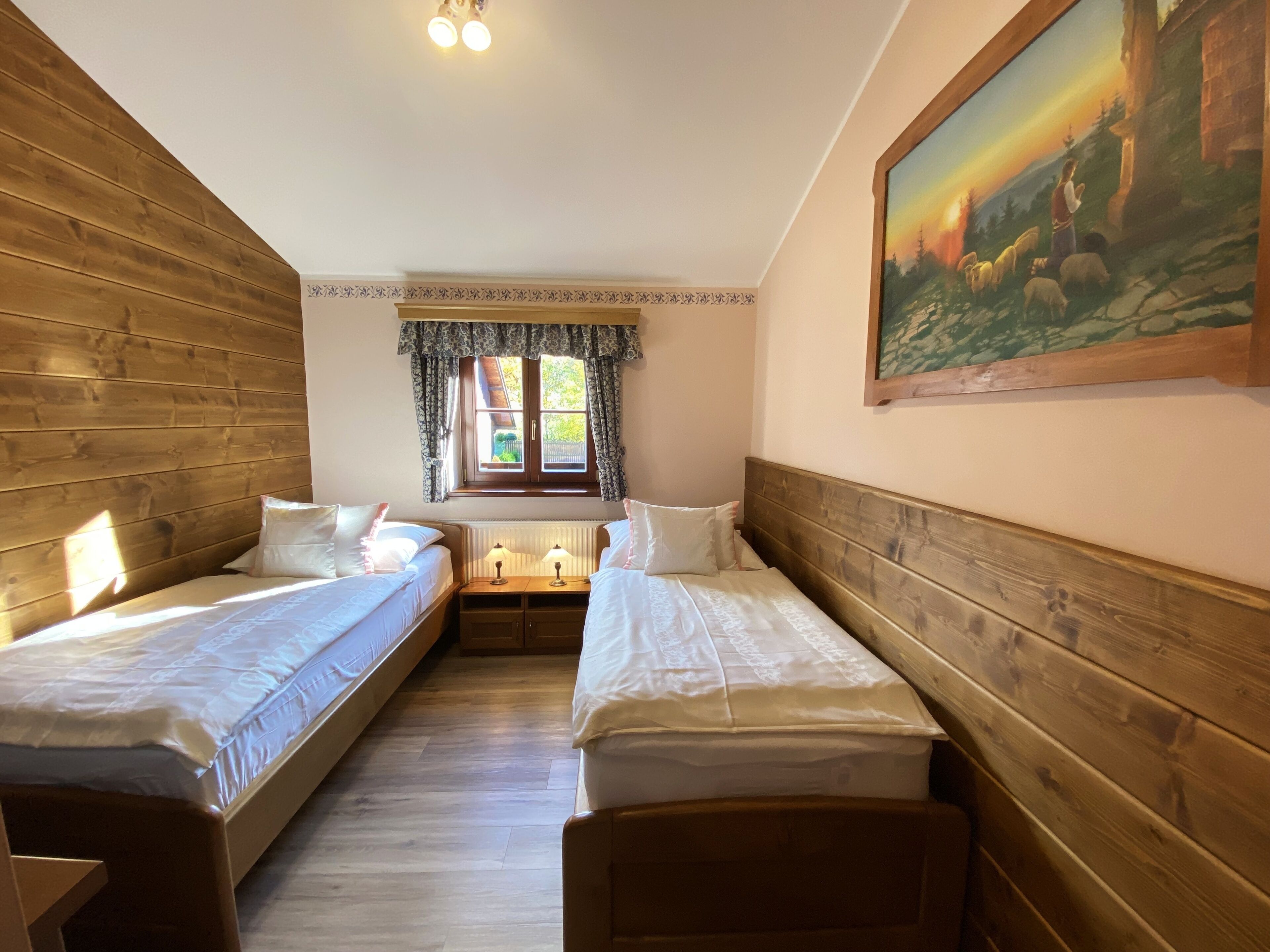 A room with two single beds, a window with curtains, a radiator, and a painting on the wall.
