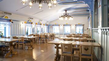 A spacious dining area with wooden tables and chairs, large windows, and decorative ceiling chandeliers.