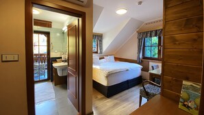 A bedroom with a bed, a bedside table, a chair, and a window. There is a bathroom visible through an open door. - Hotel na Dolině (Trojanovice)