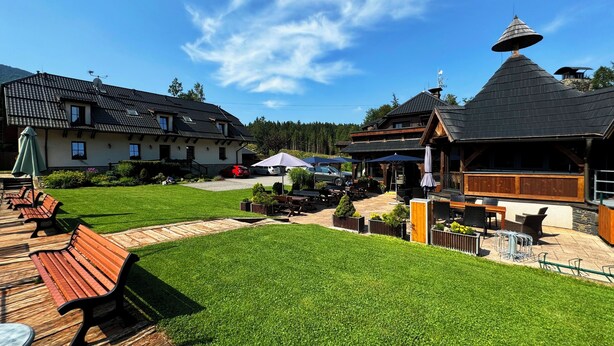 A well-maintained outdoor area with a wooden deck, benches, and a grassy lawn. - Hotel na Dolině (Trojanovice)