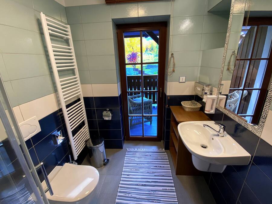 A bathroom with a white sink, a towel rack, a trash bin, and a view of the outside through a glass door.