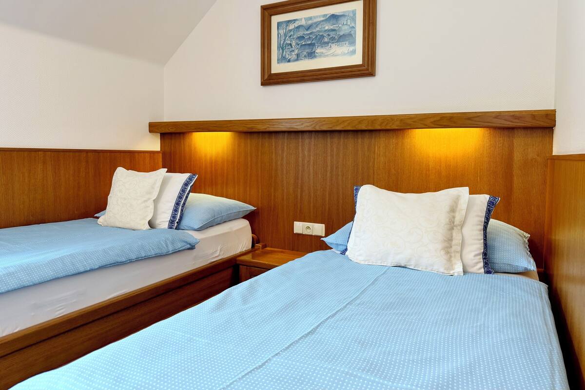 Hotellihuone, jossa on kaksi sänkyä, puiset päätyosat ja seinällä kehystetty taulu.