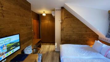 Een hotelkamer met houten wanden, een bed, een bureau met een computer en een televisie waarop een landschap wordt getoond.