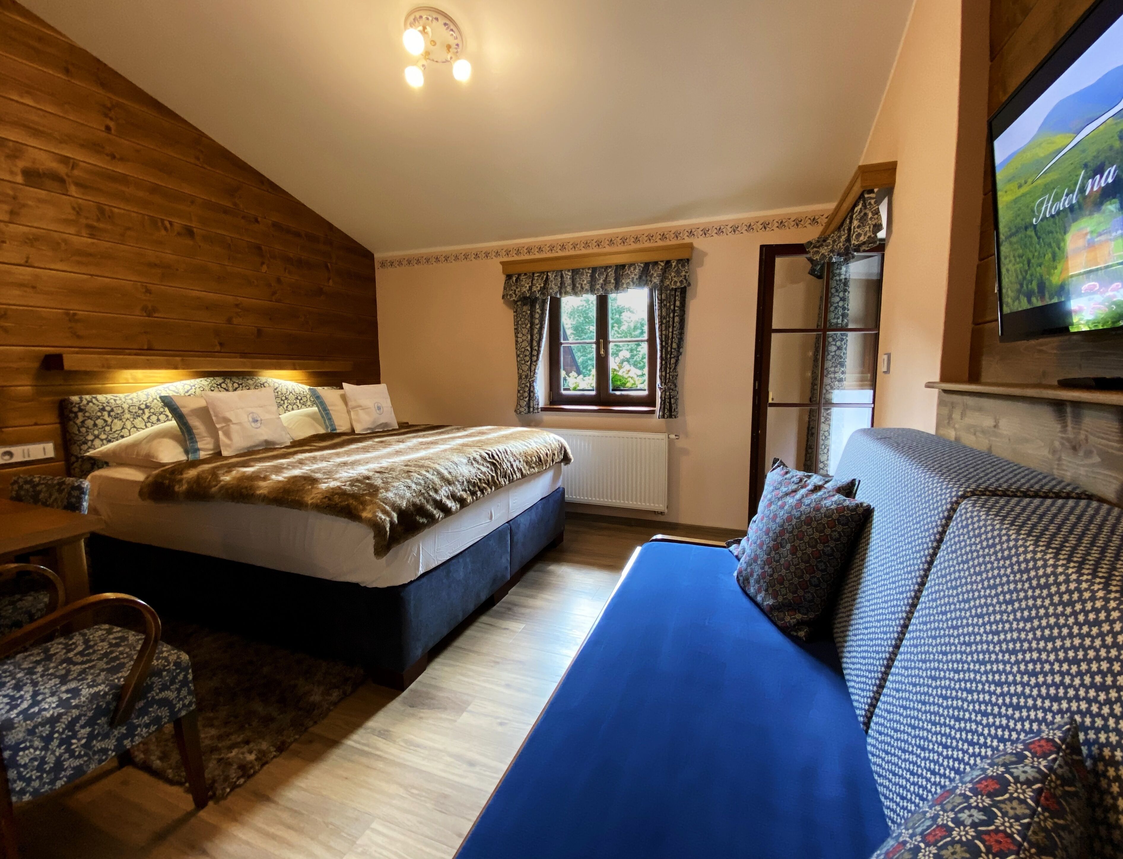 Un dormitorio acogedor con cabecera de madera, una cama grande con ropa de cama estampada, un sofá azul y un televisor en la pared.
