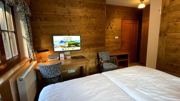 Habitación de hotel con pared de madera, cama, escritorio con silla, televisor y ventana con cortinas.