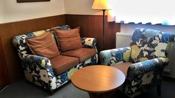 Una habitación con un sofá y sillón, una pequeña mesa de madera, una lámpara de pie y un cuadro en la pared.