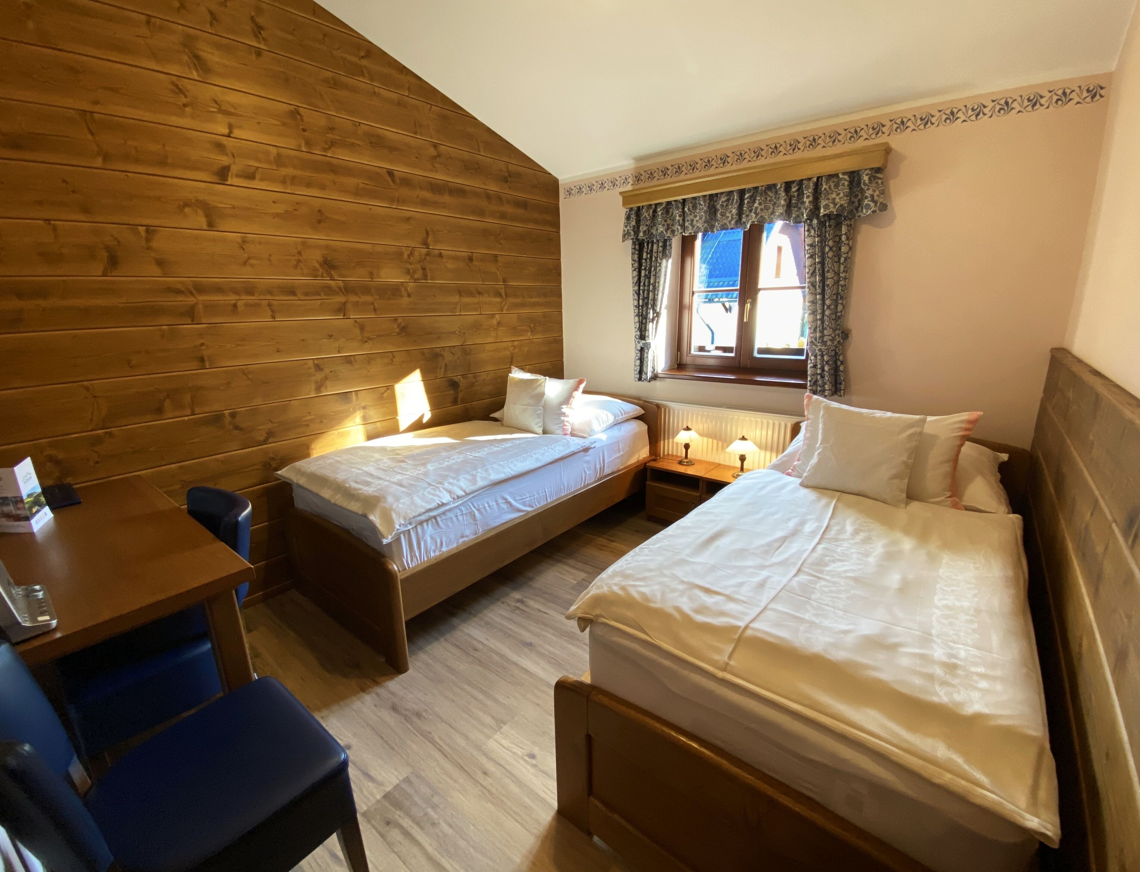 Ein Zimmer mit zwei Einzelbetten, einem Holztisch und einem Stuhl.