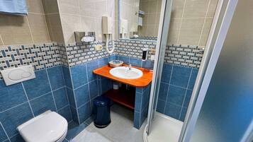 Un baño con inodoro blanco, lavabo con encimera azul, zona de ducha y suelo de baldosas.