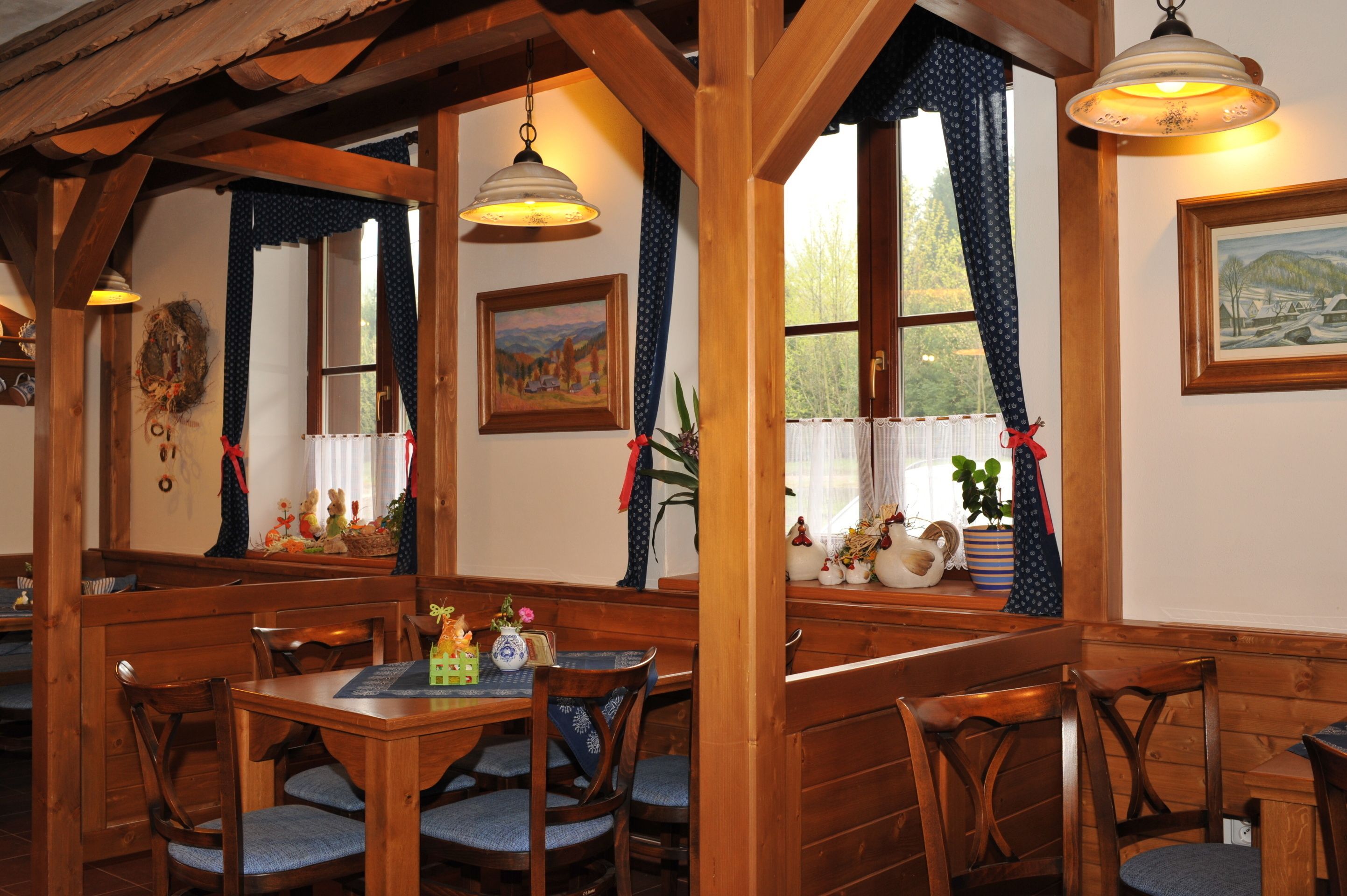 A wooden dining area with a table and chairs, a hanging light fixture, and a window with curtains.