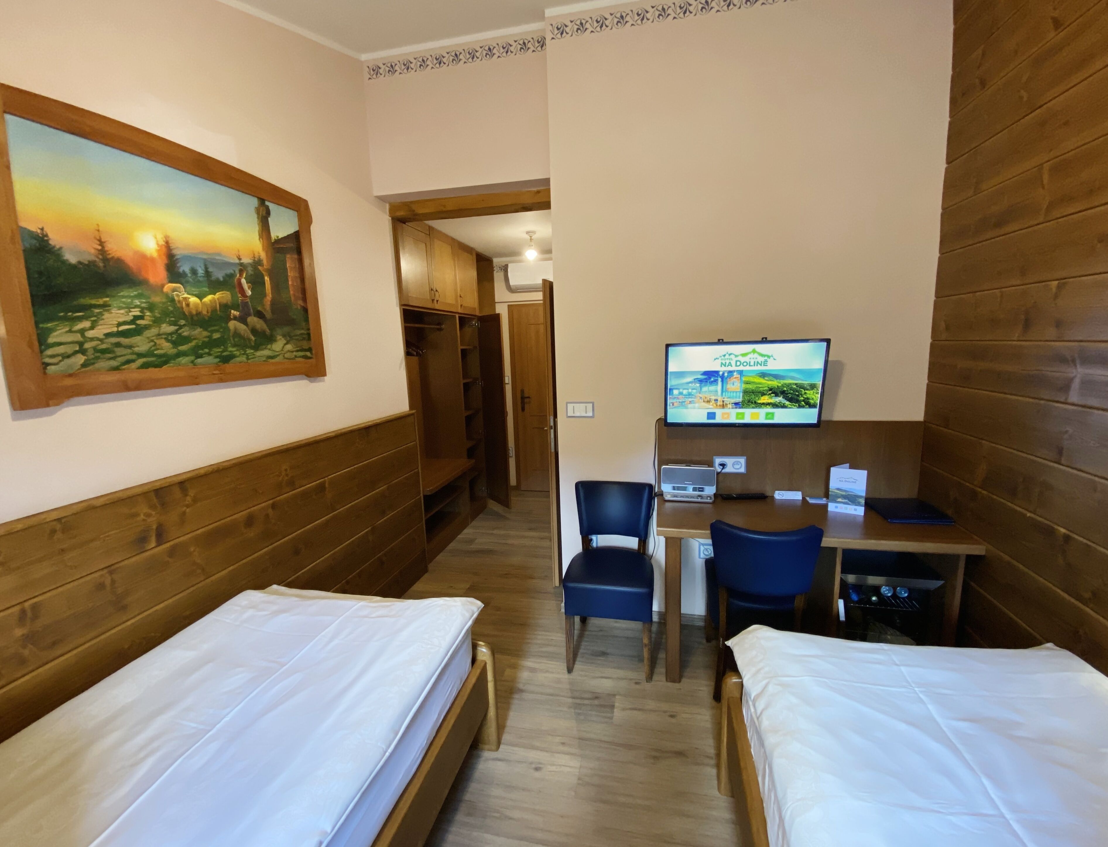Habitación de hotel con dos camas individuales, un armario de madera, televisión y un escritorio con sillas.