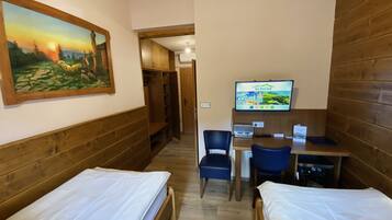 Habitación de hotel con dos camas individuales, un armario de madera, televisión y un escritorio con sillas.