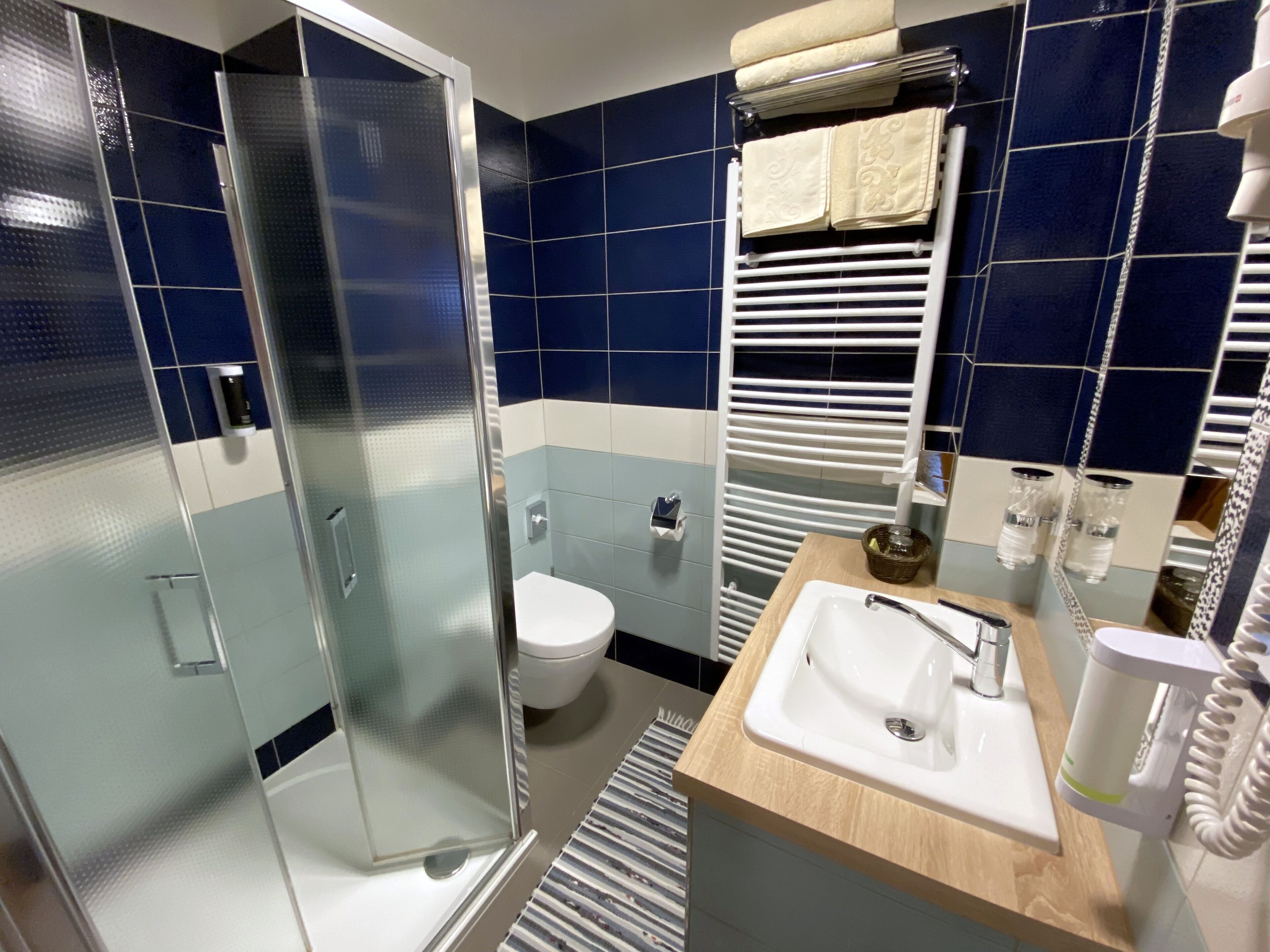 A modern bathroom with a glass shower enclosure, a white toilet, a sink with a mirror, and a towel rack with folded towels.