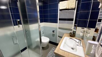A modern bathroom with a glass shower enclosure, a white toilet, a sink with a mirror, and a towel rack with folded towels.