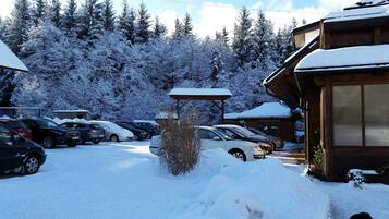 A snow-covered parking area with several cars and a wooden building with a covered porch.