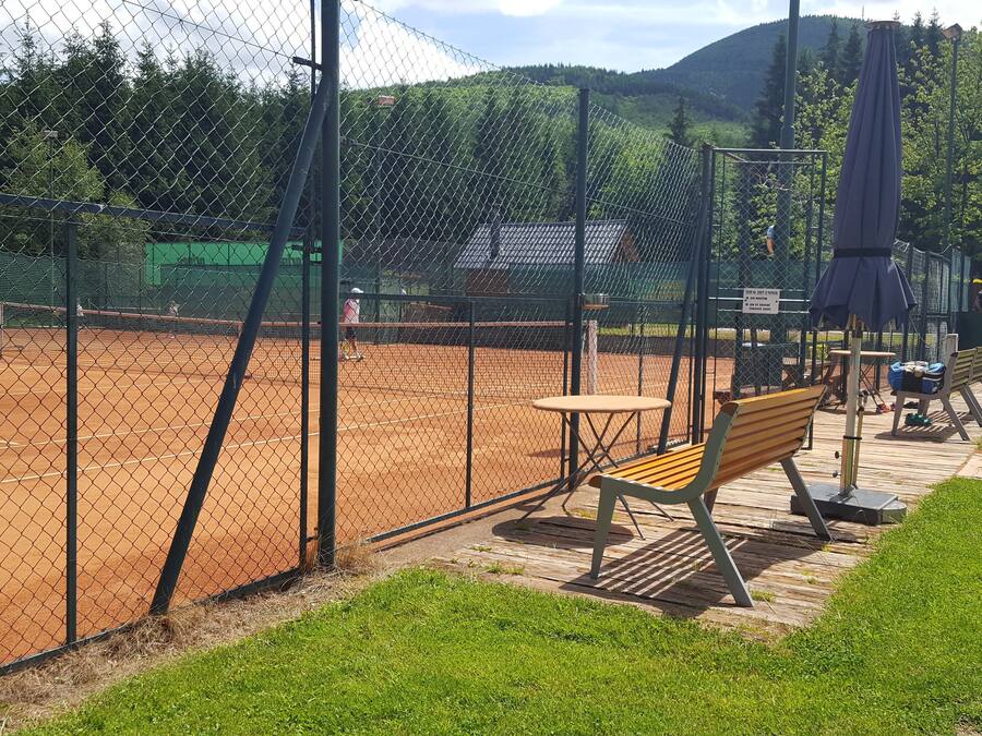 En tennisbana med ett stängsel av sammanlänkade metallkedjor, en träbänk och ett picknickbord.