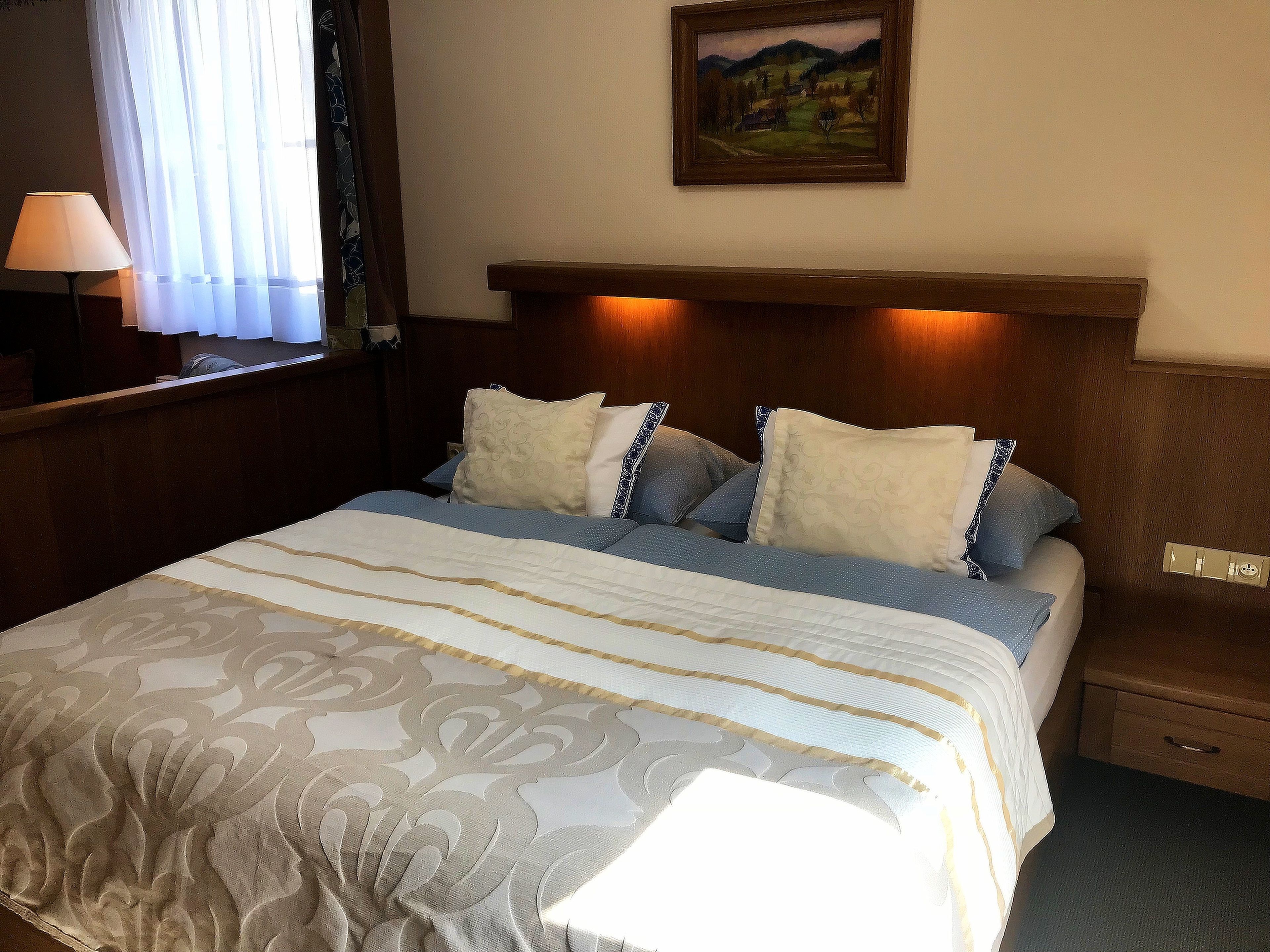 A hotel room with a large bed, a nightstand, a lamp, and a painting on the wall.