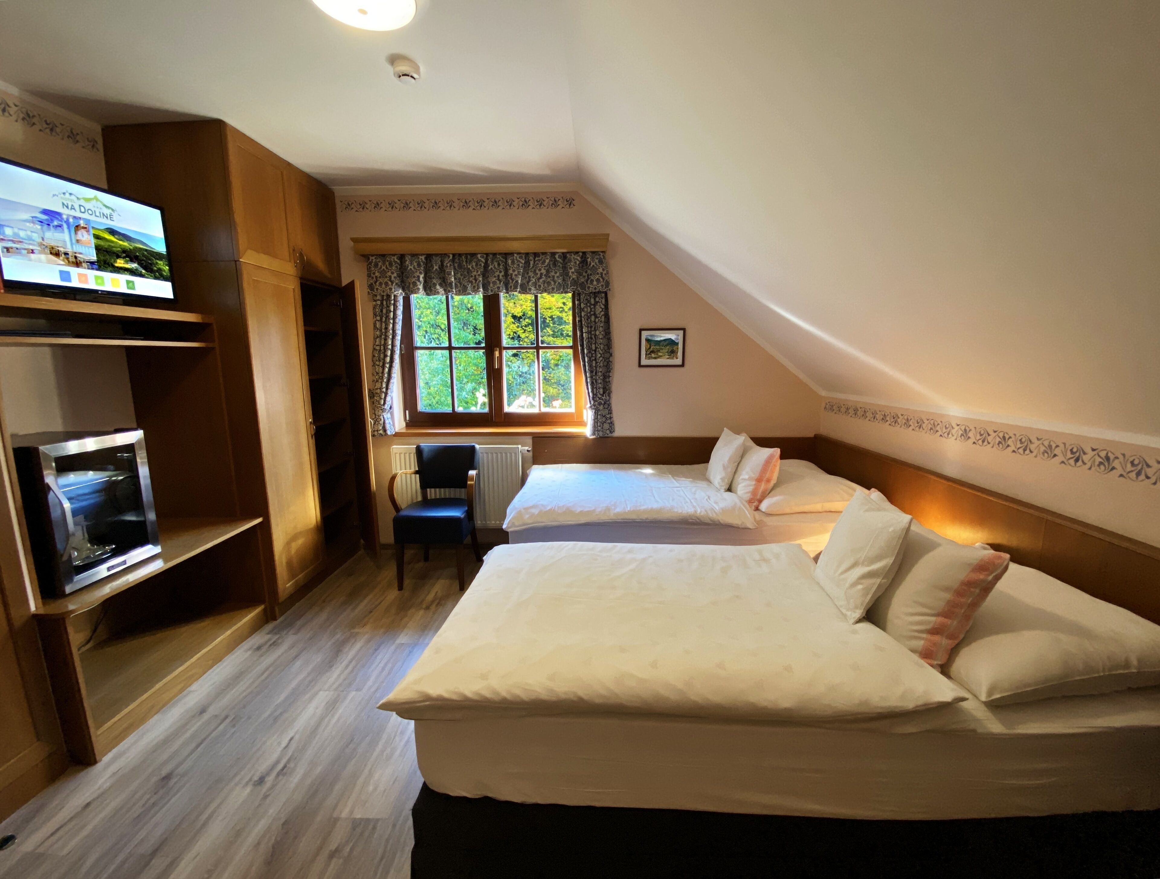 A bedroom with two beds, a desk, a television, and a window with curtains.